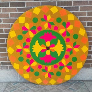 Puede incluir: Una alfombra grande, redonda y colorida con un dise&ntilde;o floral geom&eacute;trico. La alfombra presenta un fondo amarillo mostaza con formas florales y geom&eacute;tricas naranjas, amarillas, verdes y rosas. La alfombra est&aacute; colocada sobre una superficie estampada.