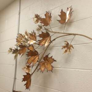 Puede incluir: Una escultura de pared de una rama con hojas de cobre. Las hojas son de varios tonos de marr&oacute;n y dorado.