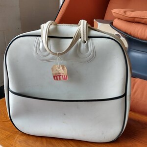 Pode incluir: Bolsa de viagem de vinil branco com acabamento preto e al&ccedil;a branca. A bolsa tem uma etiqueta de pre&ccedil;o vermelha e branca anexada que diz "MTW".