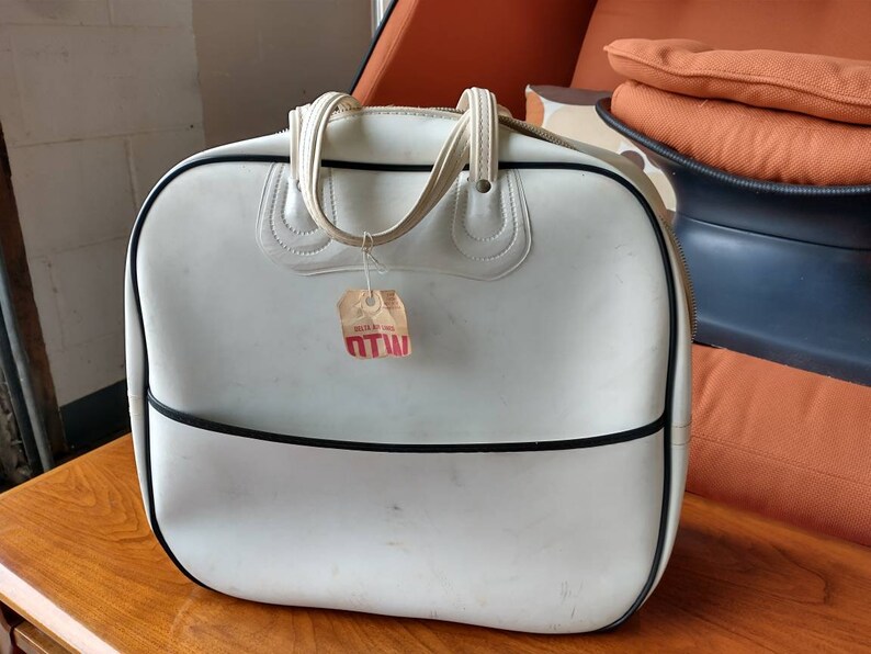 Pode incluir: Bolsa de viagem de vinil branco com acabamento preto e al&ccedil;a branca. A bolsa tem uma etiqueta de pre&ccedil;o vermelha e branca anexada que diz "MTW".