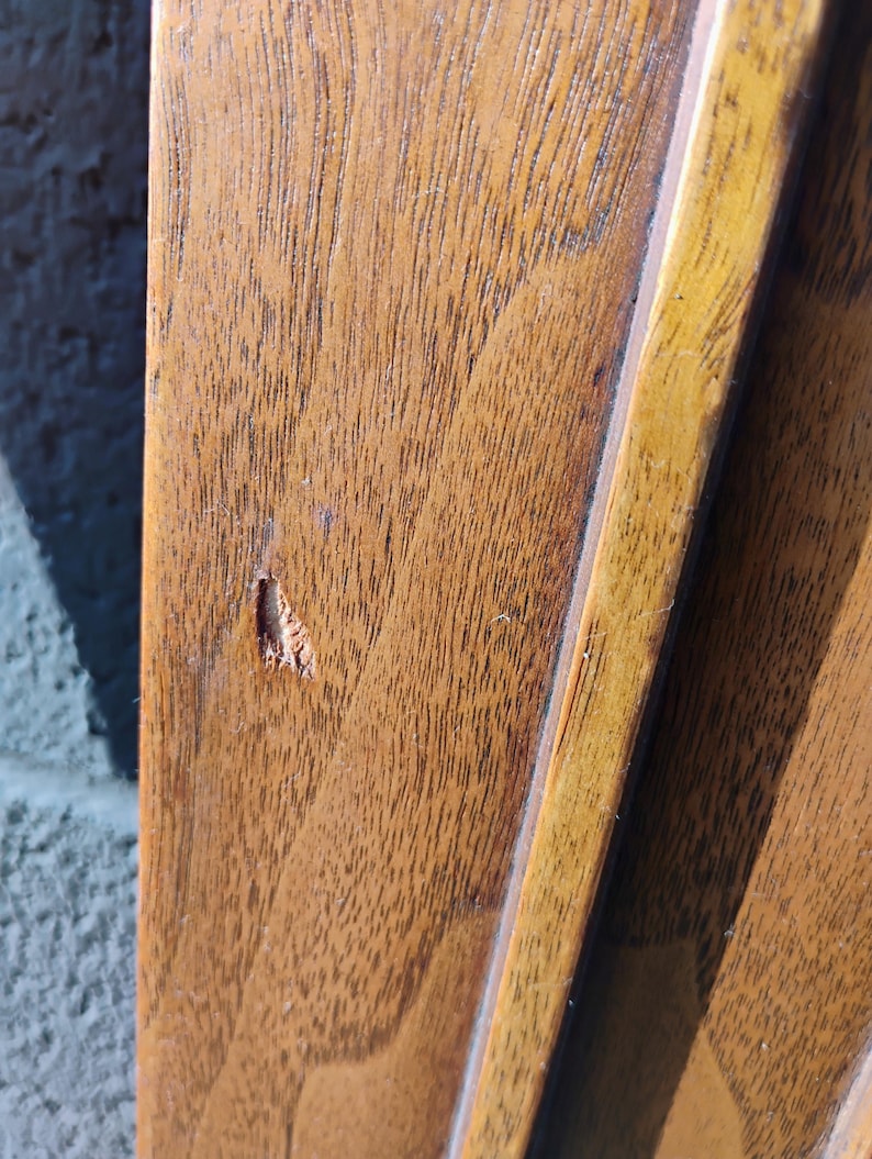 May include: Close-up of a wooden frame with a small chip in the wood. The frame is a light brown color and has a darker brown border.