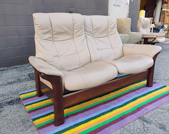 Könnte beinhalten: Ein Zweisitzer-Sofa mit cremefarbenem Lederbezug und gesteppten Paneeldetails. Das Sofa wird von einem dunkelbraunen Holzrahmen mit geschwungenen Armlehnen und stabilen Beinen getragen, die eine strukturierte Basis für die Polstersitze bilden.