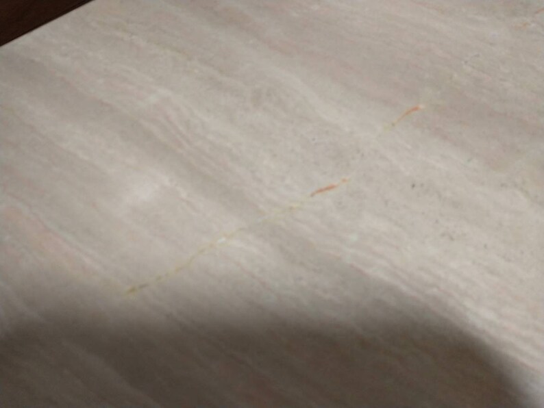 May include: A close-up of a light-colored, textured surface with subtle veining and streaks. The surface has a neutral color palette with hints of beige, cream, and light pink, creating a natural, organic appearance. The surface appears to be made of stone.
