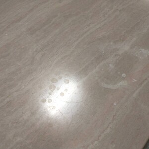 May include: A close-up of a light brown, textured surface with subtle streaks and variations in color. The surface has several small, light-colored spots and a few thin cracks. The lighting creates a soft, diffused glow across the surface.