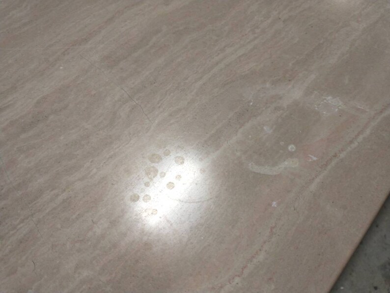 May include: A close-up of a light brown, textured surface with subtle streaks and variations in color. The surface has several small, light-colored spots and a few thin cracks. The lighting creates a soft, diffused glow across the surface.