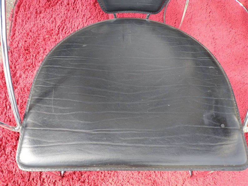 May include: Black leather chair seat with a curved shape and a chrome frame.
