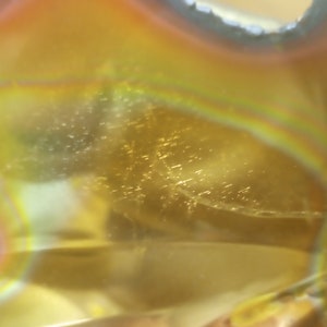 Puede incluir: Primer plano de un objeto de vidrio amarillo, naranja e iridiscente con una superficie texturizada. El vidrio tiene una forma circular con un agujero en el centro.