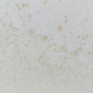 Puede incluir: Primer plano de una tela blanca con manchas marrones dispersas. Las manchas var&iacute;an en tama&ntilde;o y densidad, creando una apariencia texturizada. La tela parece ligeramente arrugada.