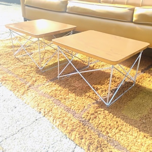 May include: Two square side tables with light brown wooden tops and white metal wire bases featuring a cross-hatch design. The tables have smooth, flat surfaces and are supported by thin, interconnected metal rods that form a geometric structure.