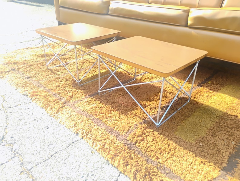 May include: Two square side tables with light brown wooden tops and white metal wire bases featuring a cross-hatch design. The tables have smooth, flat surfaces and are supported by thin, interconnected metal rods that form a geometric structure.