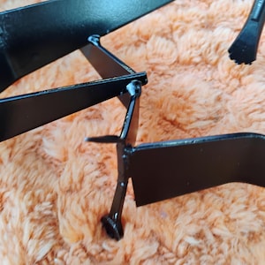 May include: Close-up of a black metal object with geometric shapes and sharp angles. The object appears to be a decorative piece or part of a larger structure, with a matte finish and visible weld points.
