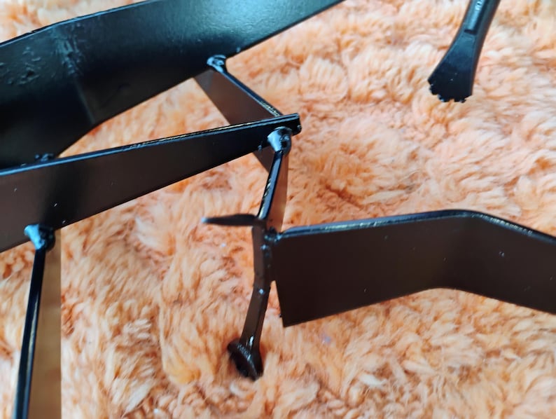 May include: Close-up of a black metal object with geometric shapes and sharp angles. The object appears to be a decorative piece or part of a larger structure, with a matte finish and visible weld points.