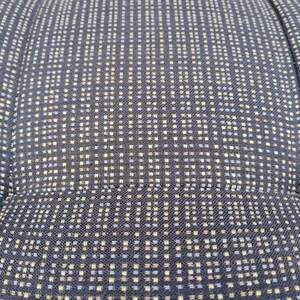 K&ouml;nnte beinhalten: Ein dunkelblauer Stoff mit einem sich wiederholenden Gittermuster aus kleinen hellblauen und beigen quadratischen Punkten. Das Textil weist eine sichtbare Webstruktur auf, wobei vertikale und horizontale N&auml;hte eine gesteppte Optik erzeugen.