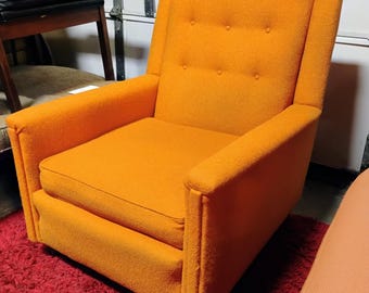 Könnte beinhalten: Ein orangefarbener Mid-Century-Moderner Sessel mit hohem Rücken und Knopfdetails. Der Stuhl hat eine kastenförmige Form mit gepolsterten Armlehnen und einem Sitzkissen. Der Stuhl steht auf einem roten Teppich.