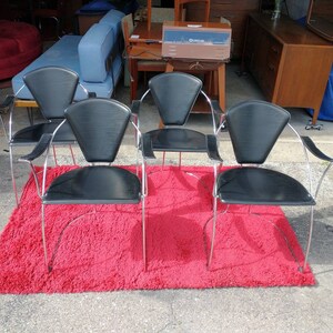 May include: Four black leather chairs with chrome frames and fan-shaped backs. The chairs are arranged on a red shag rug.