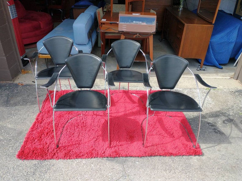 May include: Four black leather chairs with chrome frames and fan-shaped backs. The chairs are arranged on a red shag rug.