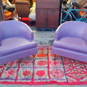 May include: Two purple chairs with rounded backs and a tufted seat. The chairs are on a red and purple rug with a geometric pattern.