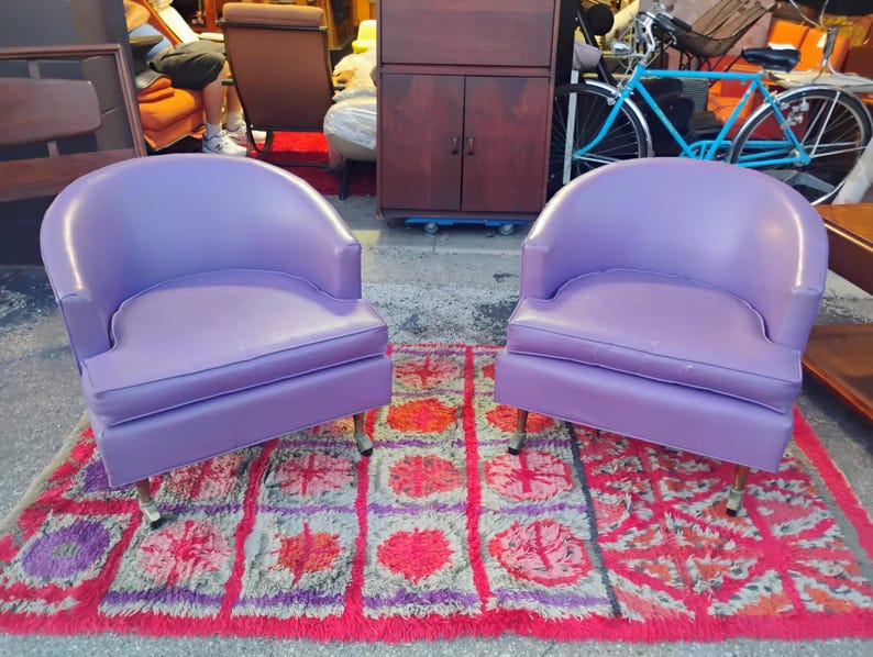 May include: Two purple chairs with rounded backs and a tufted seat. The chairs are on a red and purple rug with a geometric pattern.