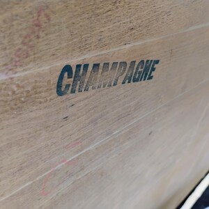 Op de afbeelding: Close-up van een houten oppervlak met het woord "CHAMPAGNE" in zwarte letters gedrukt.