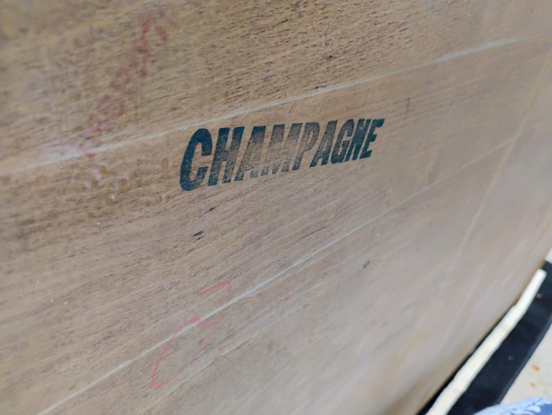 Op de afbeelding: Close-up van een houten oppervlak met het woord "CHAMPAGNE" in zwarte letters gedrukt.
