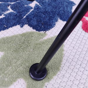 May include: Close-up of a black metal chair leg with a round black foot pad. The chair leg is resting on a white and green patterned rug.