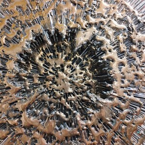 Puede incluir: Una escultura de pared circular con un dise&ntilde;o texturizado y abstracto. La escultura est&aacute; hecha de metal y tiene un acabado bronce. La superficie est&aacute; cubierta de l&iacute;neas y crestas elevadas, creando un efecto din&aacute;mico y llamativo.