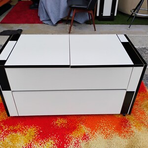 May include: A white two-drawer chest with black trim. The chest is sitting on a colorful rug.