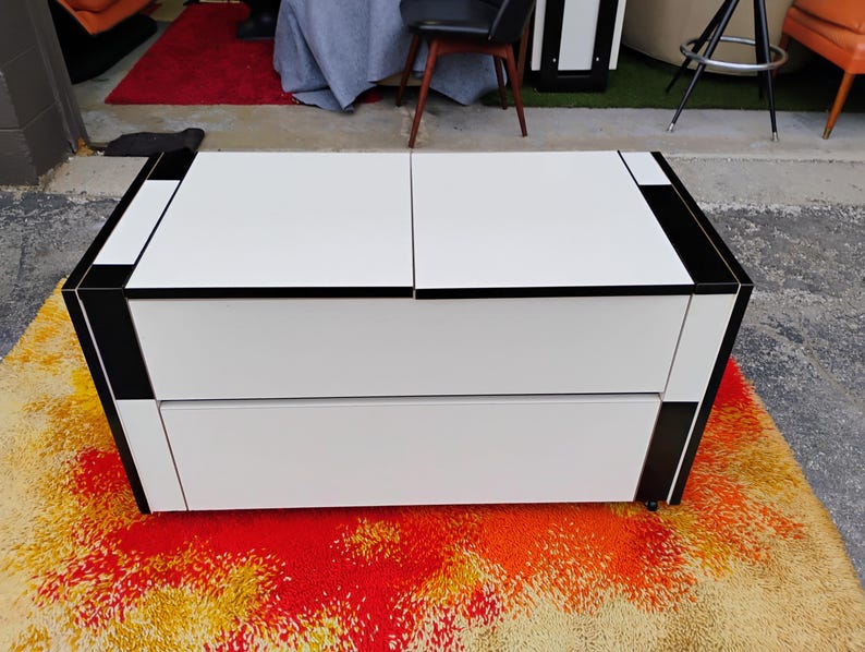 May include: A white two-drawer chest with black trim. The chest is sitting on a colorful rug.