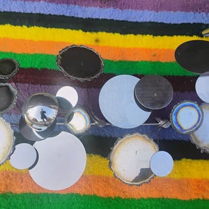 May include: A wall sculpture featuring a collection of circular mirrors and polished agate slices in shades of black, white, and iridescent blue. The pieces are arranged on a metal frame, creating a reflective and textured composition of varied sizes.