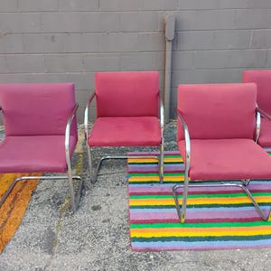 May include: A set of four armchairs featuring deep pink upholstered seats and backrests supported by continuous polished chrome tubular metal frames. Each chair has a cantilevered base design with curved armrests and a square backrest.