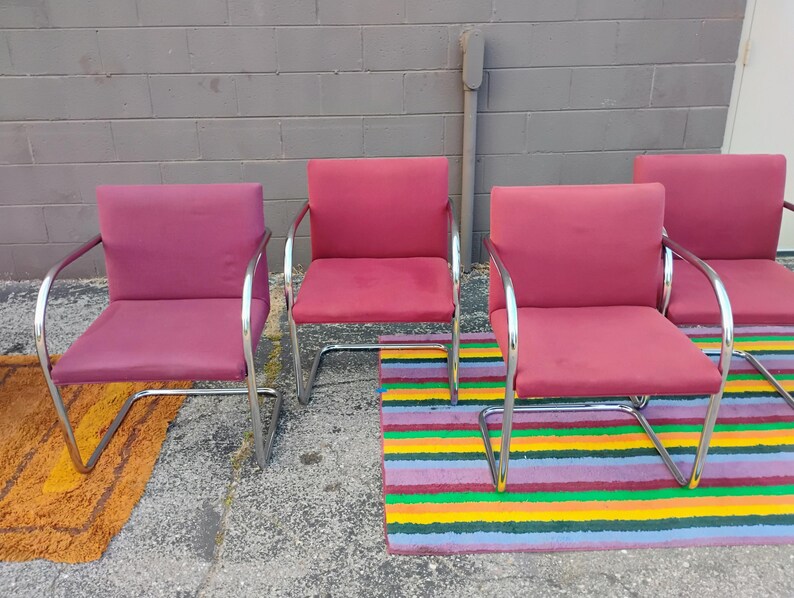 May include: A set of four armchairs featuring deep pink upholstered seats and backrests supported by continuous polished chrome tubular metal frames. Each chair has a cantilevered base design with curved armrests and a square backrest.