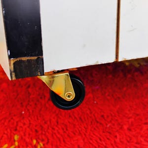 May include: A close-up of a gold caster wheel with a black rubber tire. The wheel is attached to a piece of furniture.
