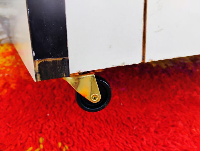 May include: A close-up of a gold caster wheel with a black rubber tire. The wheel is attached to a piece of furniture.