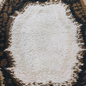 May include: A close-up of a brown and white shag rug with a circular pattern. The centre of the rug is white and the outer edge is brown.