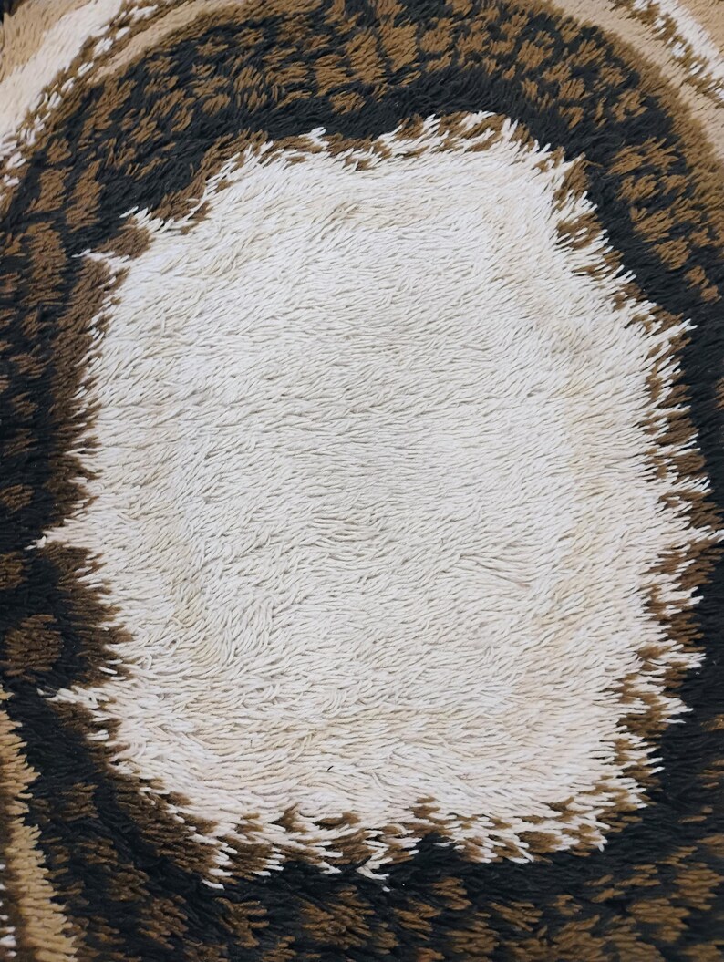 May include: A close-up of a brown and white shag rug with a circular pattern. The centre of the rug is white and the outer edge is brown.