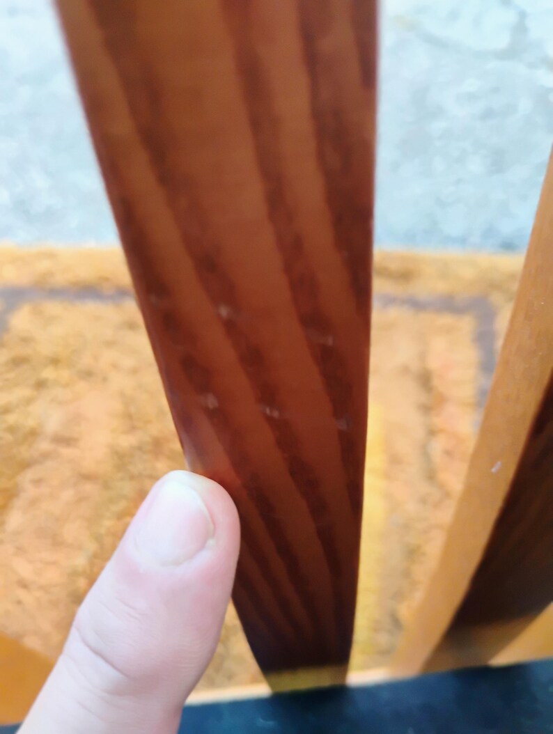 May include: A vertical wooden slat with a smooth, polished finish and visible brown wood grain patterns. The slat is positioned upright, showcasing the natural texture and warm, medium-toned color of the wood material in a clear, focused view.