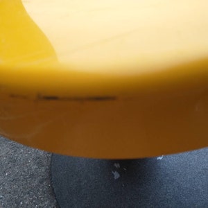 May include: A yellow, round, plastic stool with a black base. The stool has a few scratches on the surface.