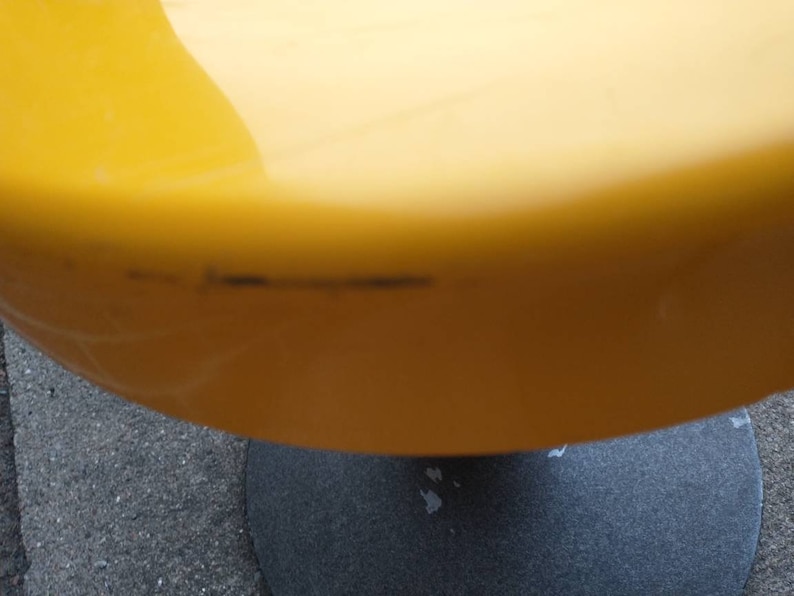 May include: A yellow, round, plastic stool with a black base. The stool has a few scratches on the surface.