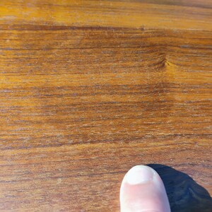 Op de afbeelding: Een close-up van een glad, gepolijst houten oppervlak met een warme, medium bruine tint met zichtbare horizontale nerfpatronen en natuurlijke houtknopen. De textuur ziet er consistent uit en is afgewerkt met een lichte glans.