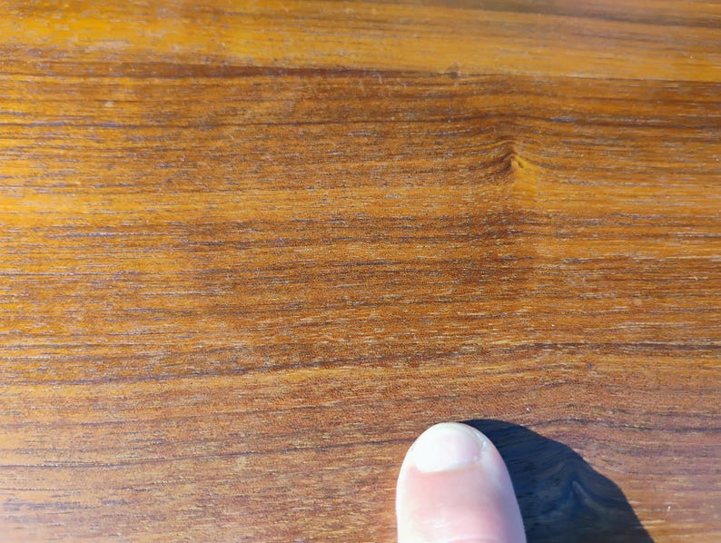 Op de afbeelding: Een close-up van een glad, gepolijst houten oppervlak met een warme, medium bruine tint met zichtbare horizontale nerfpatronen en natuurlijke houtknopen. De textuur ziet er consistent uit en is afgewerkt met een lichte glans.
