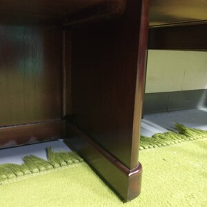 Pu&ograve; includere: Primo piano della parte inferiore di una scrivania in legno marrone scuro con un tappeto verde sotto.