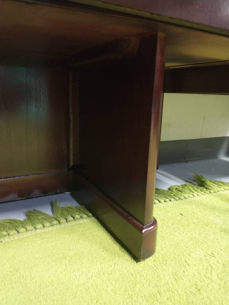 Pu&ograve; includere: Primo piano della parte inferiore di una scrivania in legno marrone scuro con un tappeto verde sotto.
