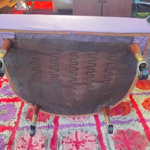 May include: Purple velvet armchair with wooden legs and wheels. The chair is flipped over, showing the underside of the seat with springs.