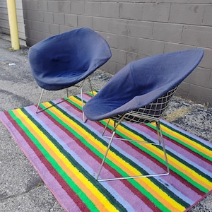 May include: Two blue fabric-covered chairs with wire grid shells and thin silver-toned metal legs. Each chair features a rounded, bowl-shaped seat design with a textured navy blue upholstery that covers the interior and exterior of the wire frame.