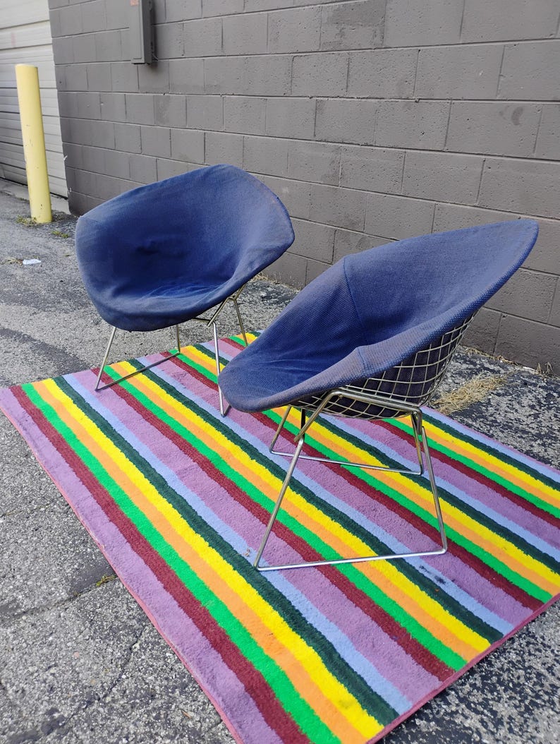 May include: Two blue fabric-covered chairs with wire grid shells and thin silver-toned metal legs. Each chair features a rounded, bowl-shaped seat design with a textured navy blue upholstery that covers the interior and exterior of the wire frame.
