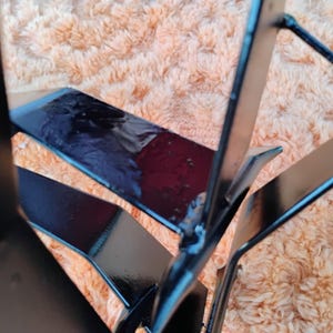 May include: Close-up of a black metal object with geometric shapes. The object has a glossy finish and appears to be made of welded metal. The background is a fuzzy, peach-colored surface.