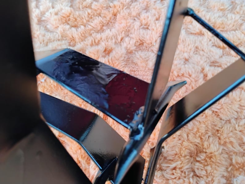 May include: Close-up of a black metal object with geometric shapes. The object has a glossy finish and appears to be made of welded metal. The background is a fuzzy, peach-colored surface.