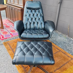 May include: A black leather lounge chair and matching ottoman set featuring a tufted button design, a high backrest with an integrated headrest, curved armrests, and a metal swivel base. The upholstery has a smooth finish with diamond patterns.