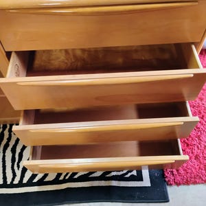Op de afbeelding: Een licht houten dressoir met vier lades. De lades zijn open, waardoor het houten interieur zichtbaar is. Het dressoir staat op een zwart-wit zebrakleurig tapijt.