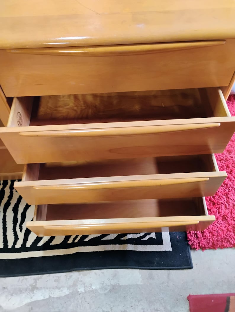 Op de afbeelding: Een licht houten dressoir met vier lades. De lades zijn open, waardoor het houten interieur zichtbaar is. Het dressoir staat op een zwart-wit zebrakleurig tapijt.
